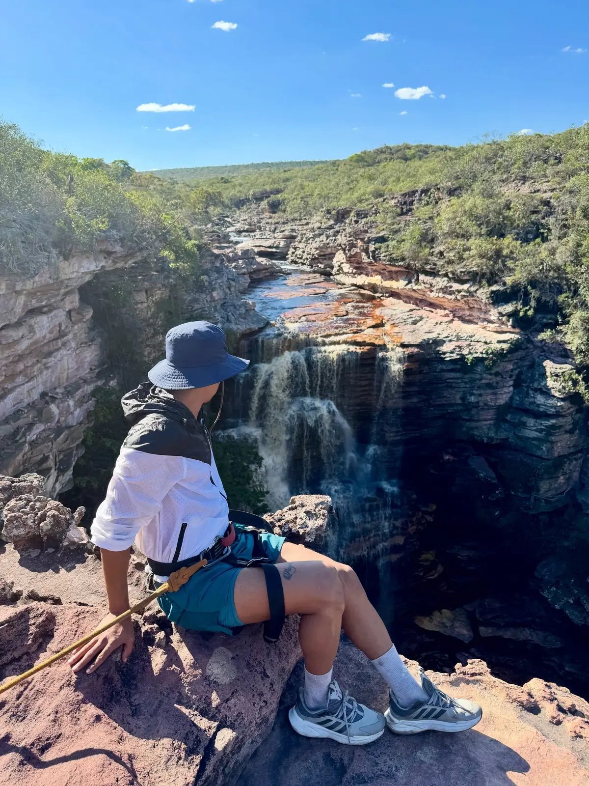 Pessoa de chapéu e cadeirinha sentada na borda de pedra, olhando a cachoeira do Poço do Diabo cair no cânion
