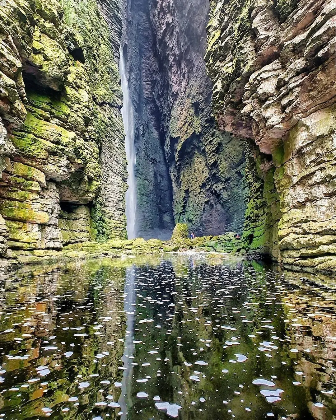 Cachoeira da Fumacinha: queda d'água alta entre paredões cobertos de musgo, refletida no poço do cânion